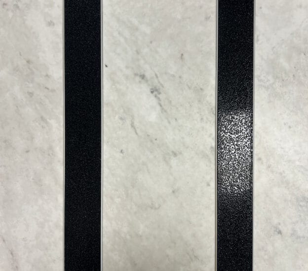 Svart aluminiumlist med halksäkert ilägg på ljust stengolv